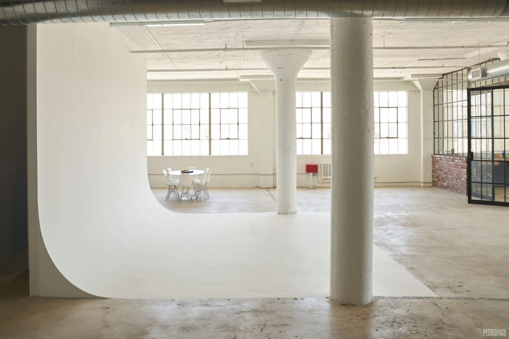 Bright, white industrial space with backdrop for production shoots, small breakout tables and a glass-enclosed conference area