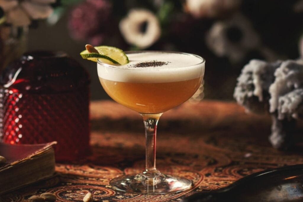 An orange colored cocktail in a coupe glass sits on a bar
