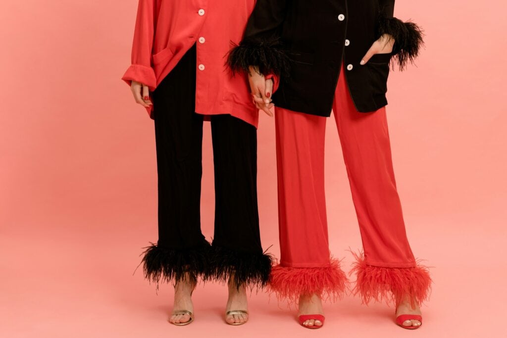 Two women from the chest down wearing glam Galentines outfits, mismatched red and black power suits and heels