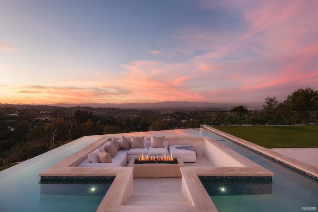 The sun sets behind a concrete, inset couch surrounded by an infinity pool