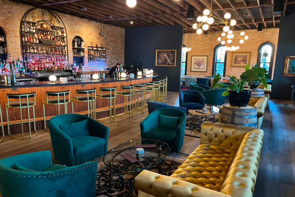 Gold and teal seating accentuate brick walls and dark accents in a bar and lounge space