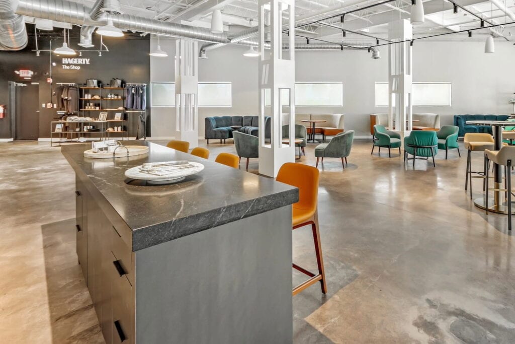 Multiple work spaces and seating areas in an open office space with white walls and columns and bright colored chairs