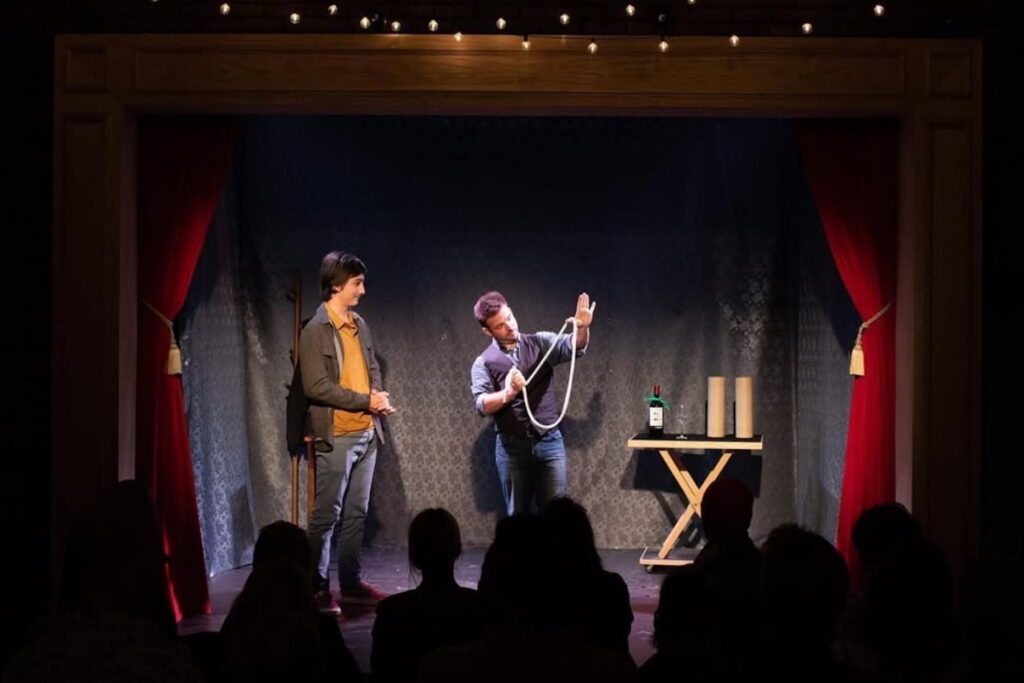 A magician on stage with an onlooker performing a magic trick