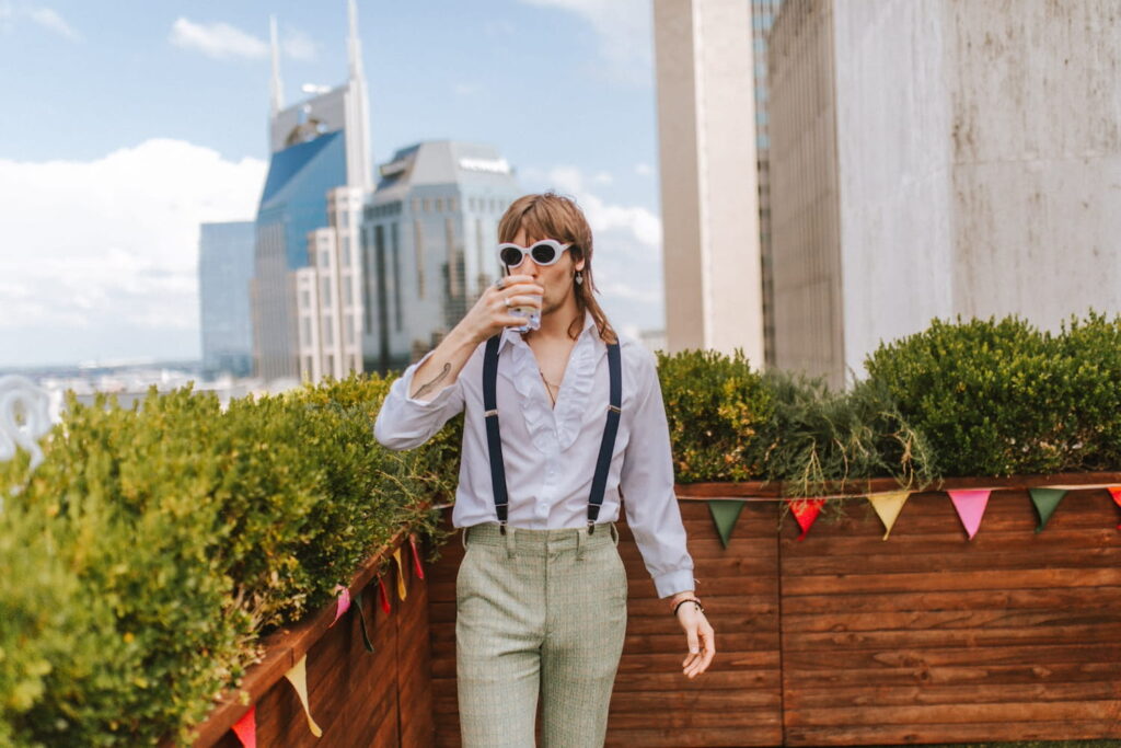 A man in suspenders drinks a cocktail on a rooftop in Nashville