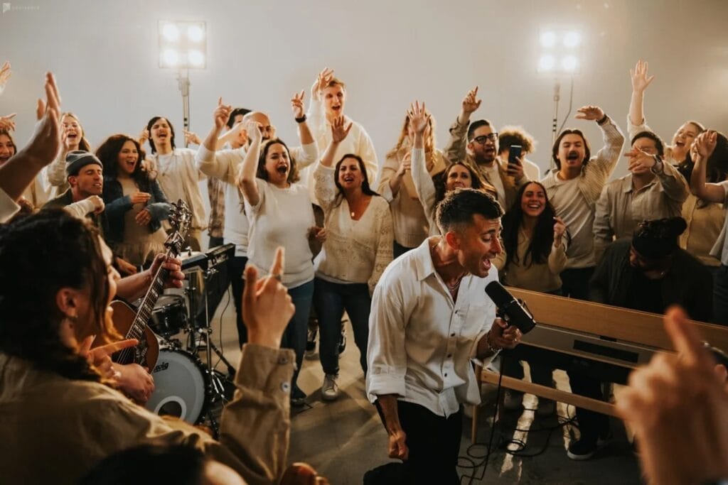 A man sings into a microphone surrounded by happy revelers
