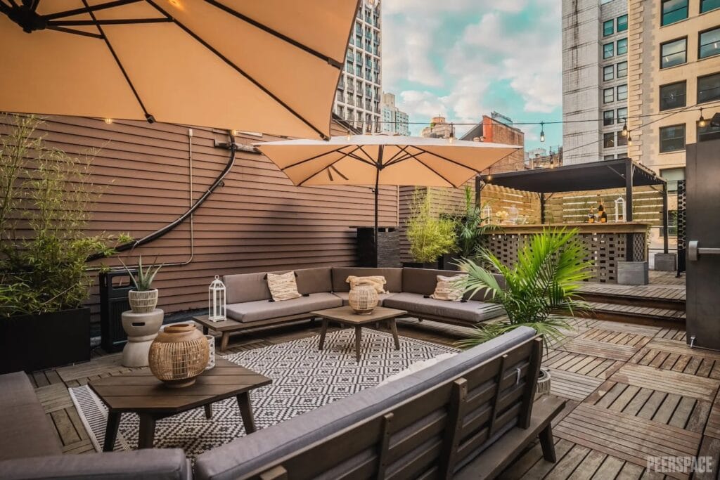 Couches, umbrellas and a covered bar area are nestled under string lights on a rooftop in the city