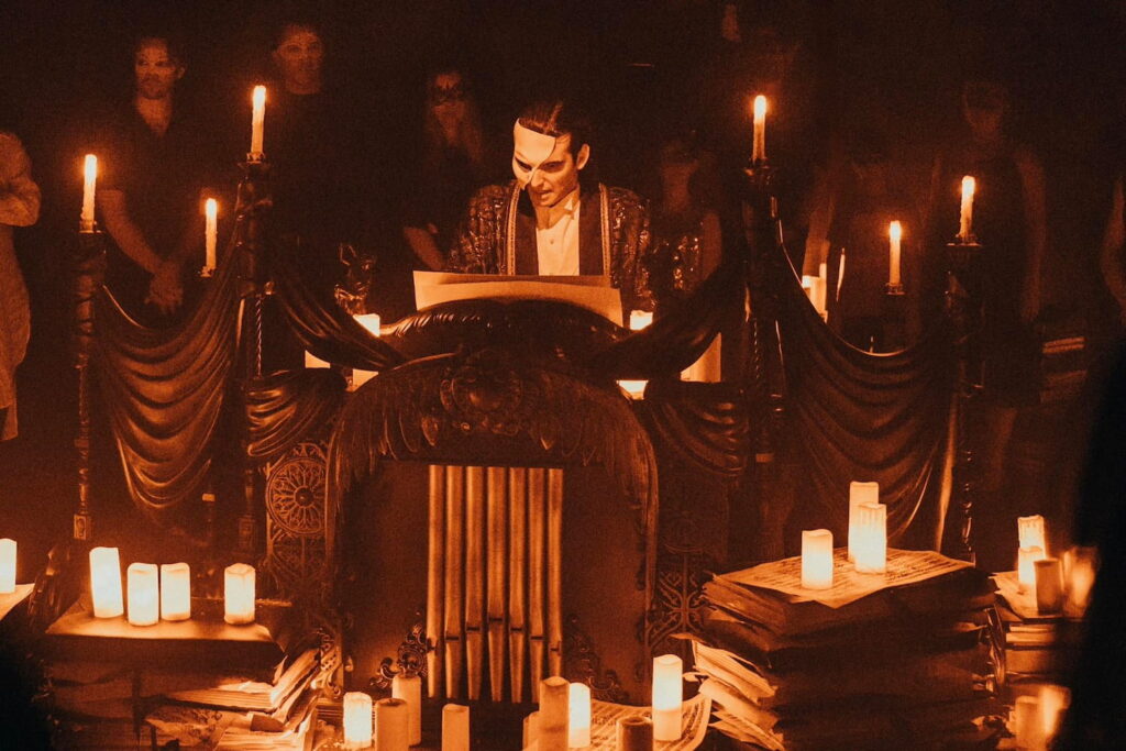 A man in a masquerade mask at a podium surrounded by candles