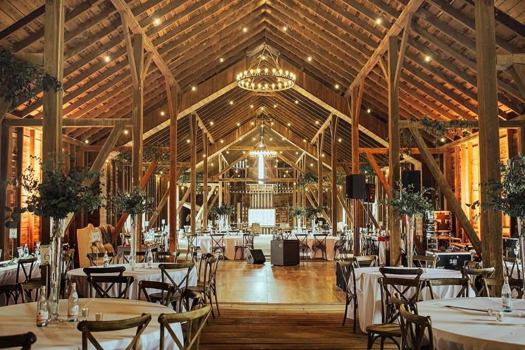 A massive barn with giant chandeliers and tall beams is decorated for a wedding reception