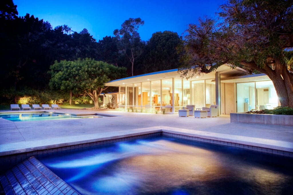 A pool and hot tub area in the backyard of a lit up Miami home at dusk