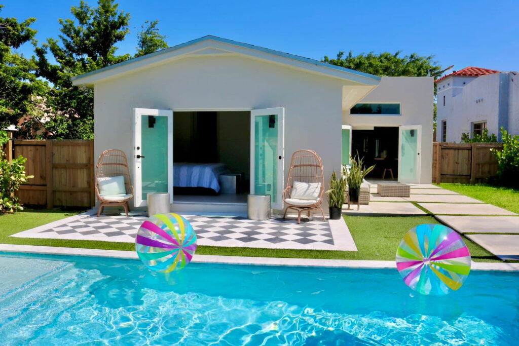 A small guest house is opened up to a pool area in a bright and sunny backyard
