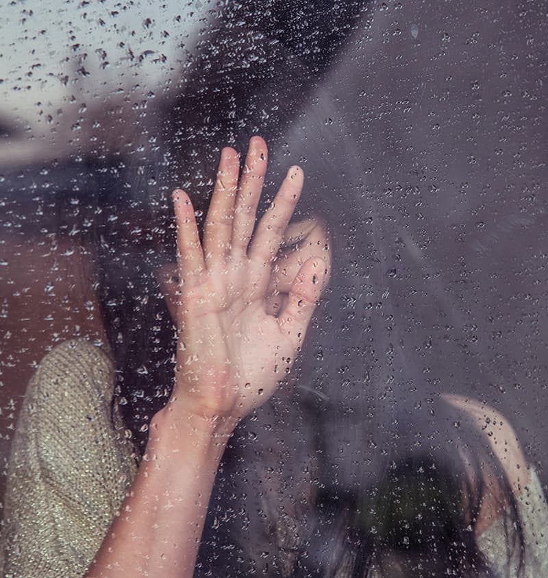 Woman standing next to window in the rain