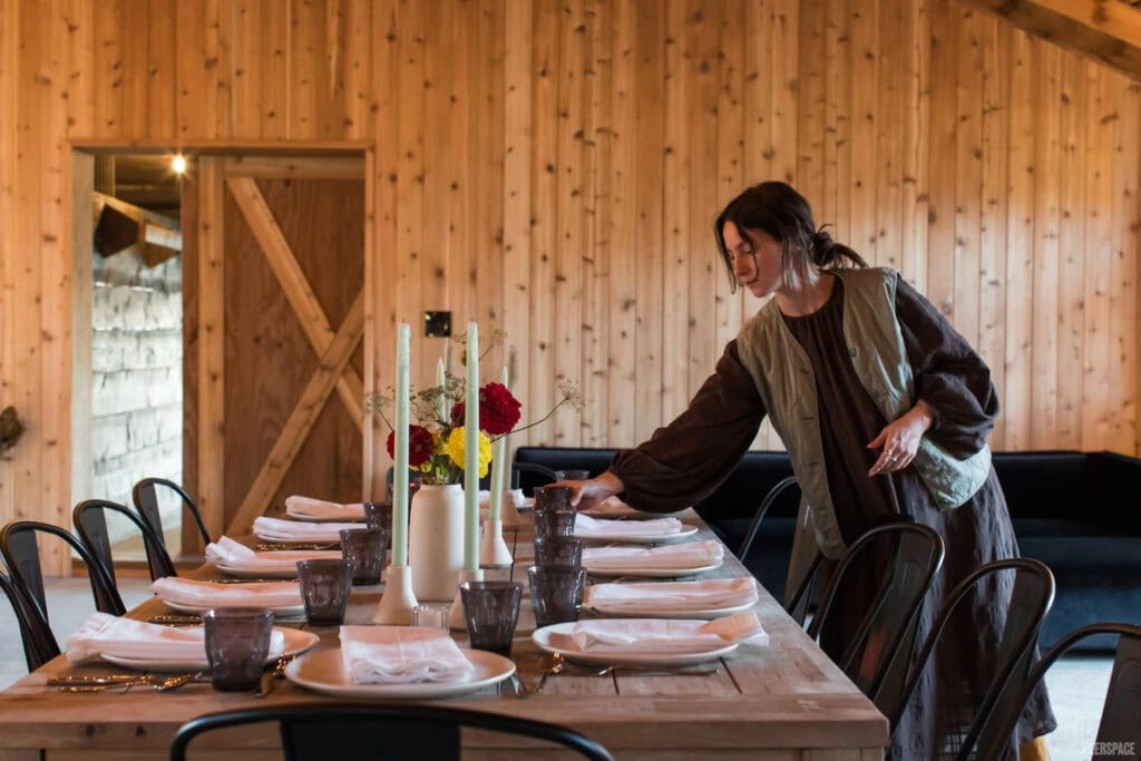 A woman sets a table inside a rustic barn