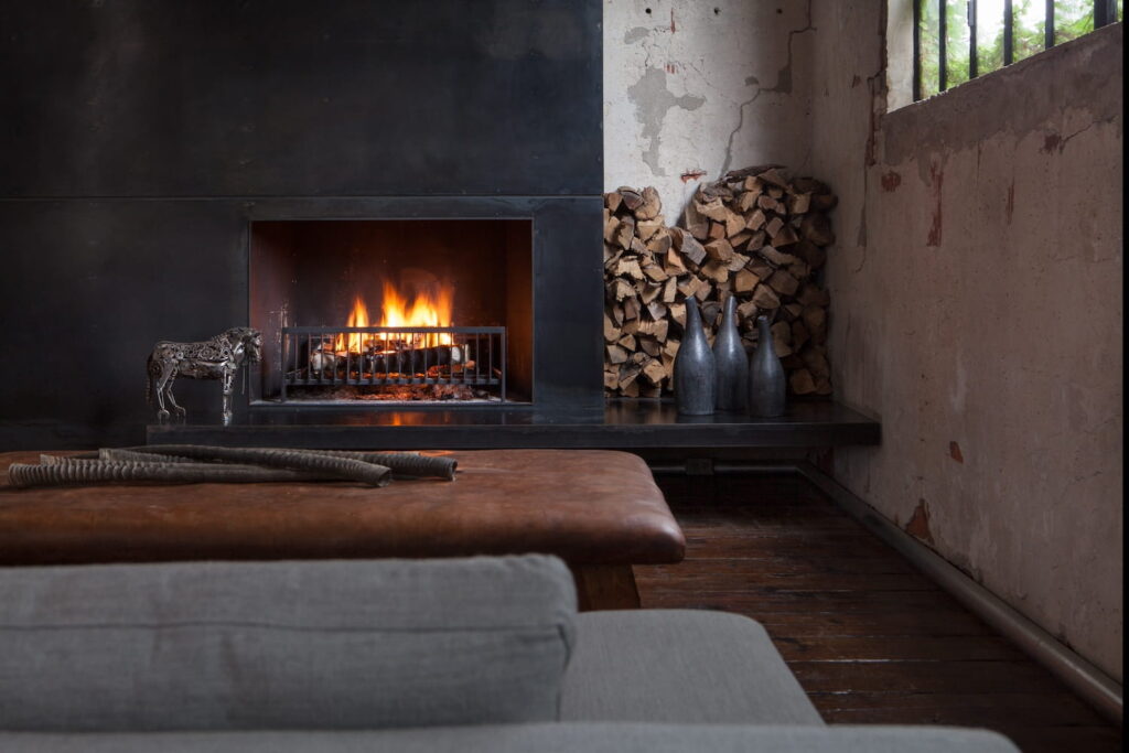 A cozy living area with a dark firelplace next to a wood pile