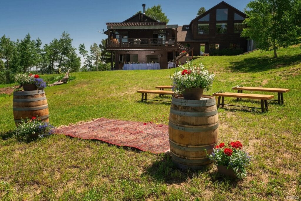 Barrels topped with floral arrangements act as a sweet wedding altar outside a beautiful mountain house