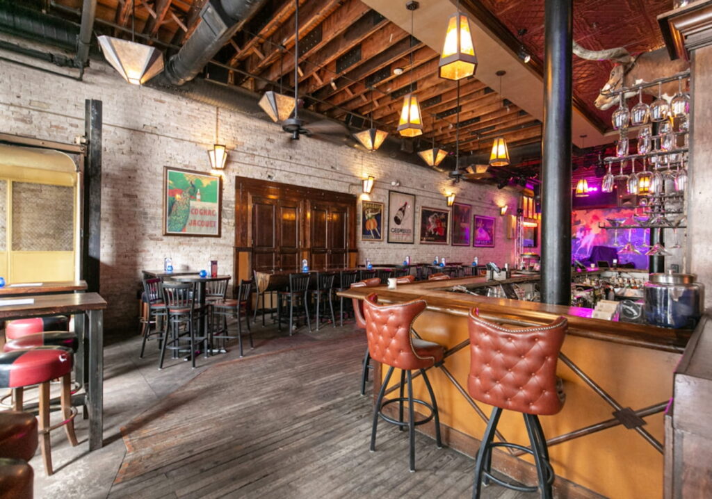 Bar area with exposed brick walls, wooden doors, tufted leather barstools and a stage in the back