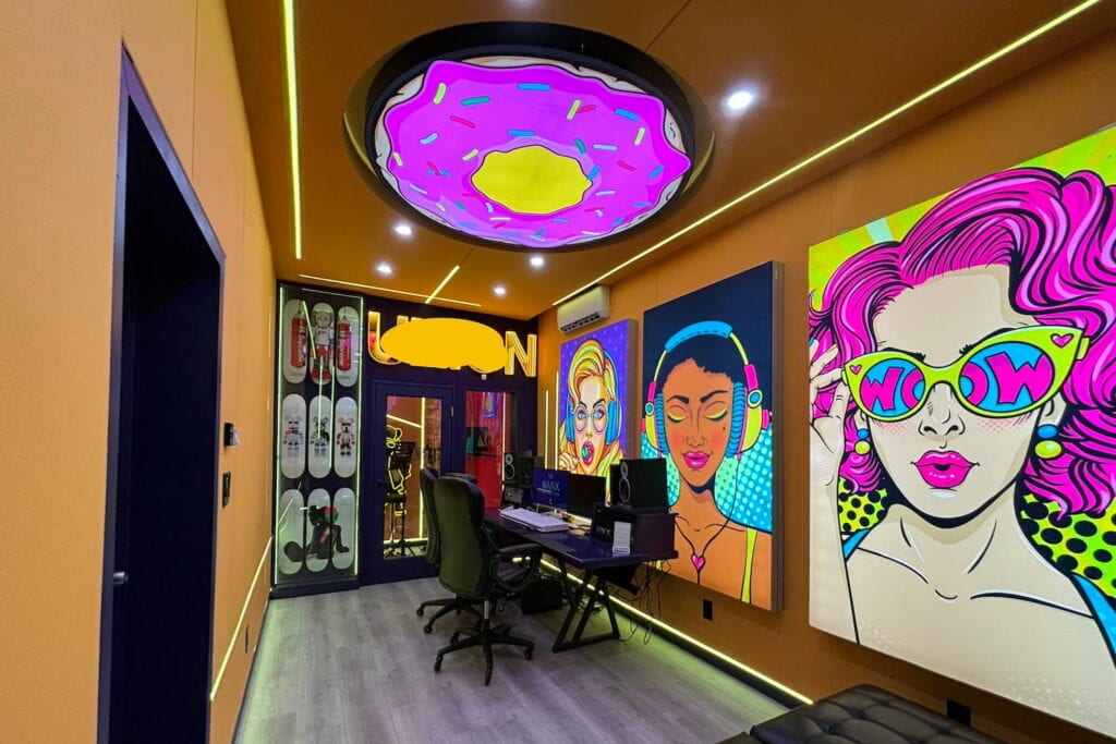 Neon pop art hangs on the walls of a small recording studio with a sound booth in back