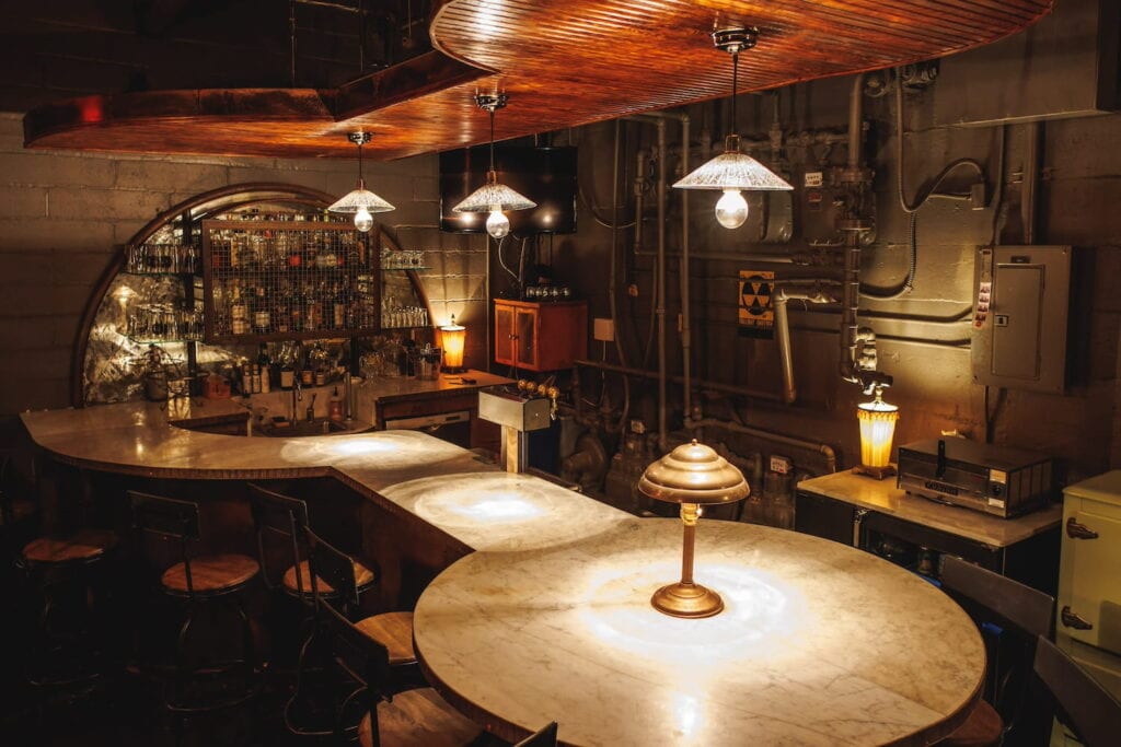 Moody lighting illuminates a basement bar with a wooden ceiling