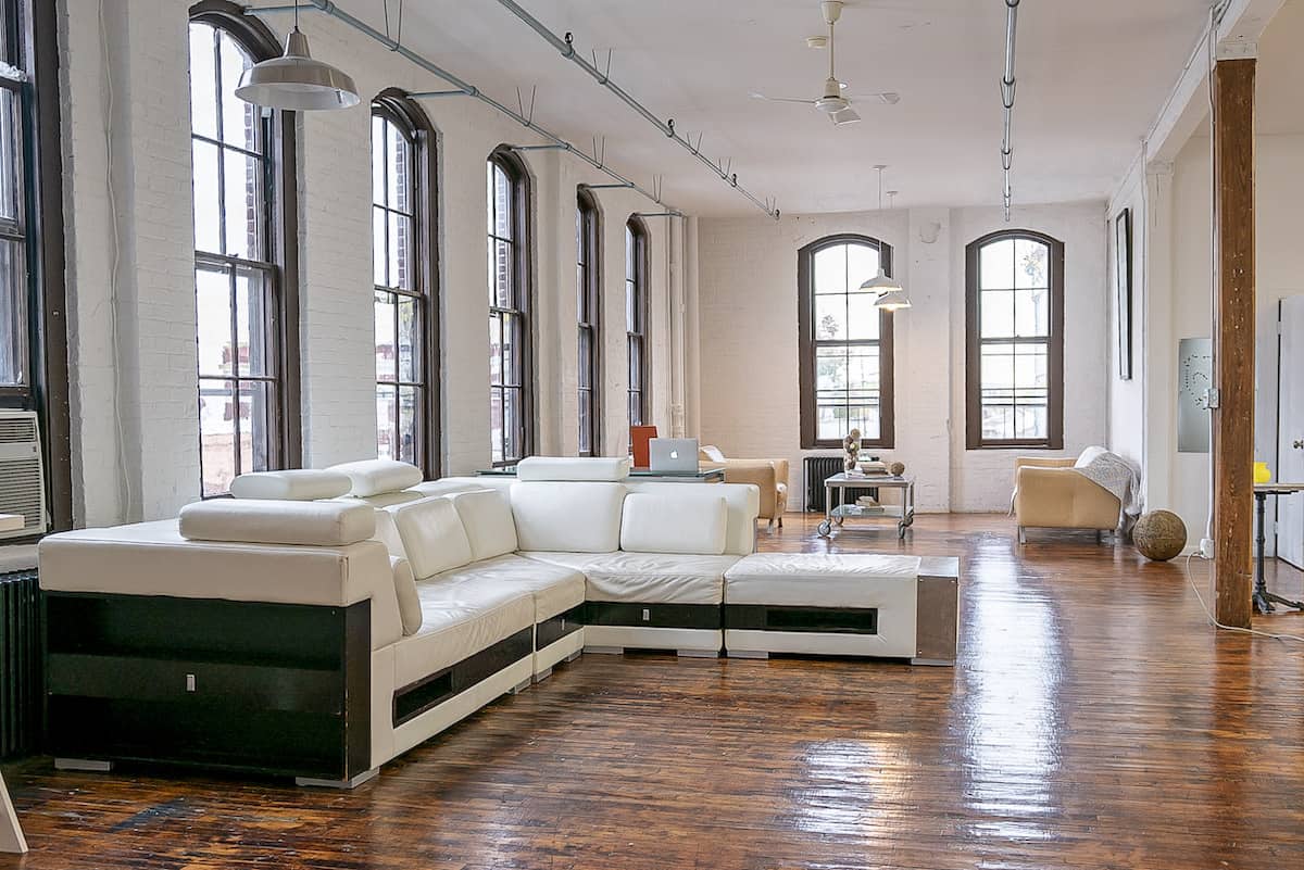 Large loft photography rental space with wooden floors, tall windows and white leather couches