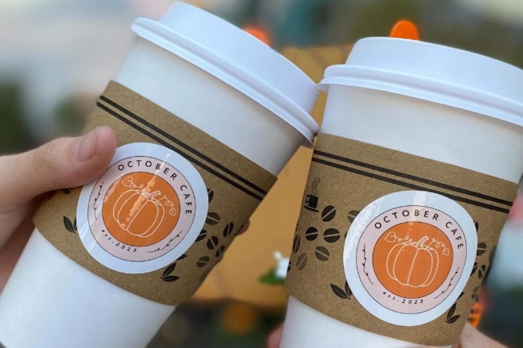 Close up shot of two coffee cups with the October Cafe logo on the sleeve