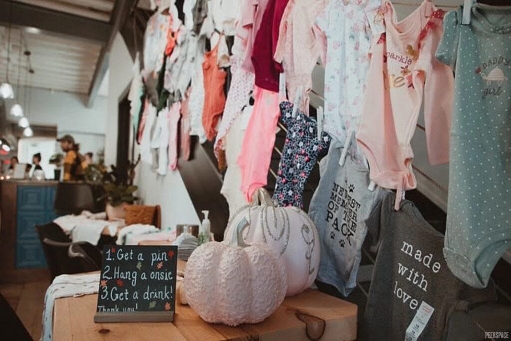 Onesies are hung on tiny clothespins against a wall at a baby event