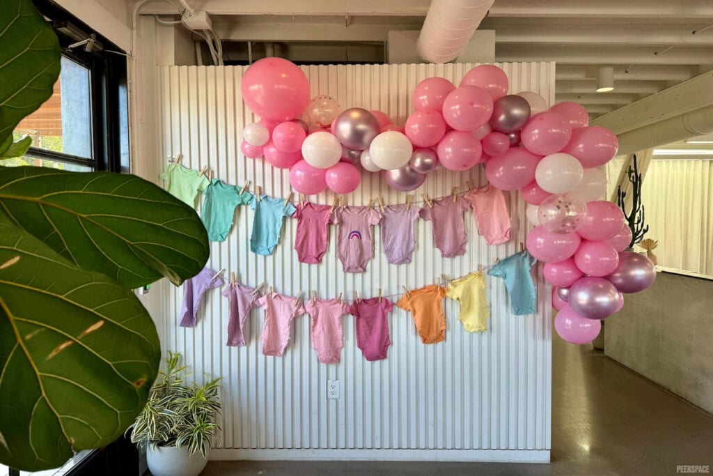 Baby onesies of all colors hang on faux clotheslines at a baby party