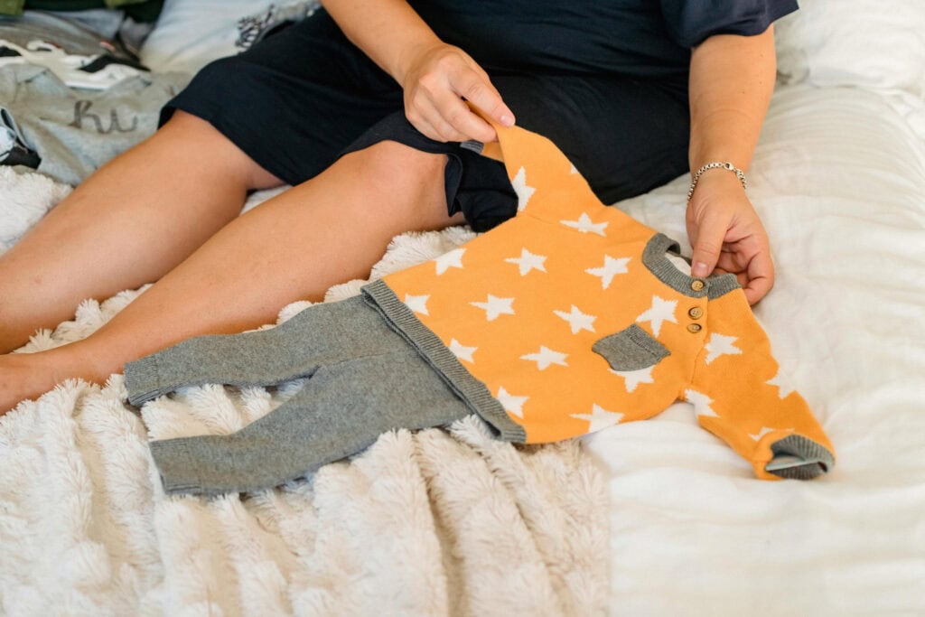 A person holds an orange and gray baby outfit with white stars on the top