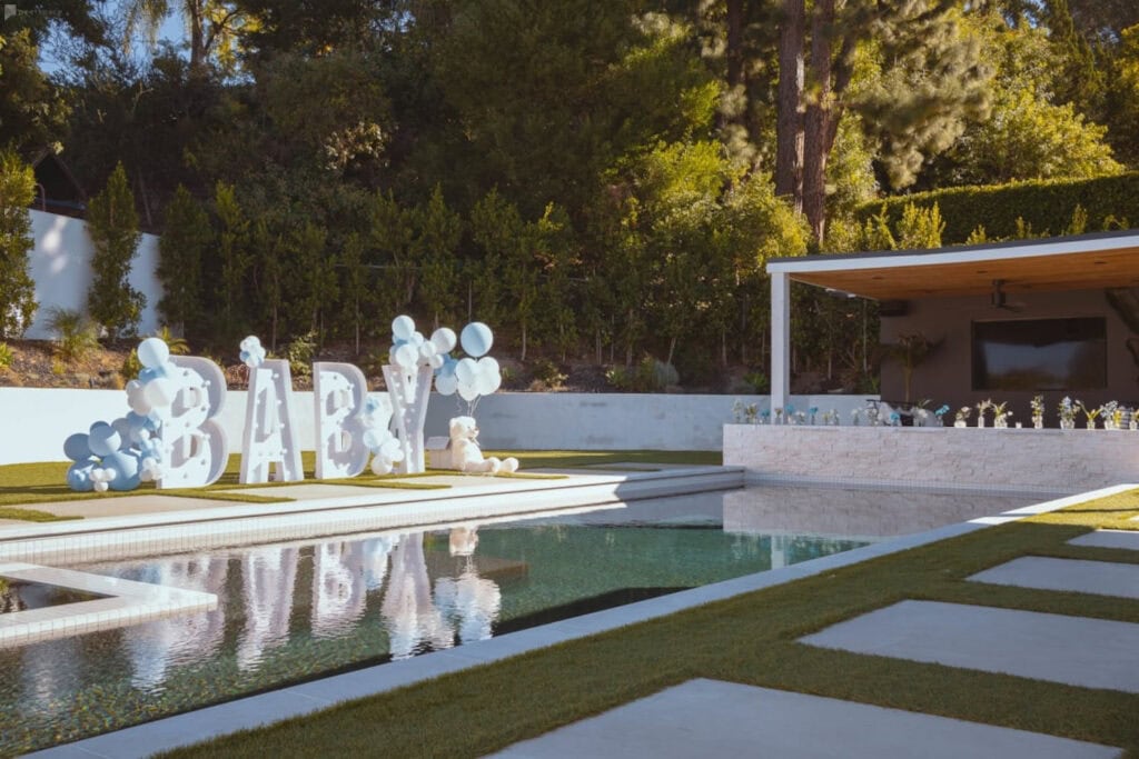 A giant baby sign sits next to a pool at an outdoor venue decorated with blue and white balloons