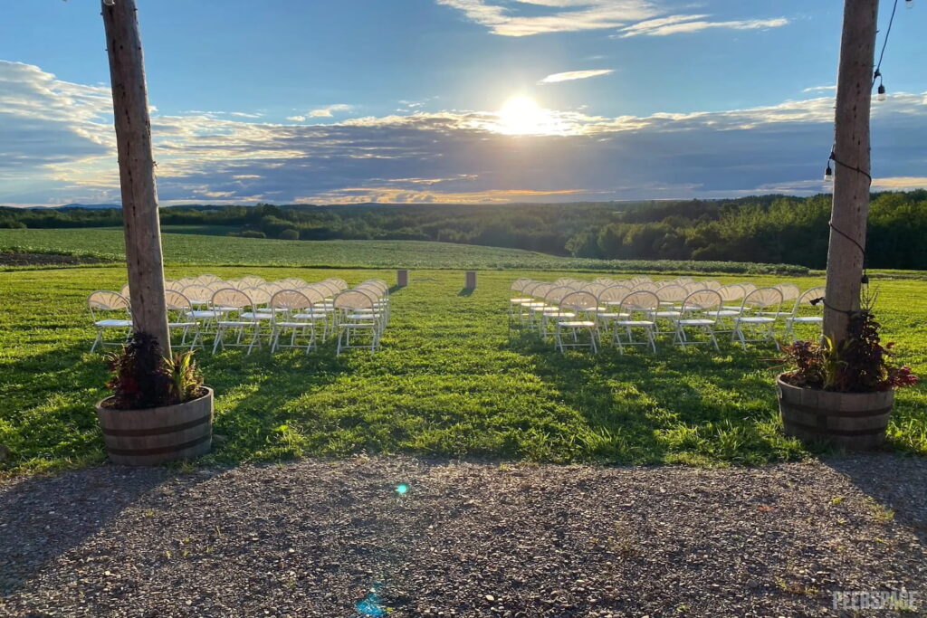 A wedding ceremony is set up in the grass of a huge field with the sun setting in the distance
