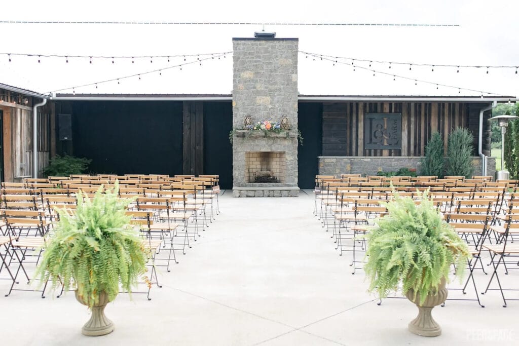 A simple wedding ceremony is set up outside with ferns and a flower-covered mantle above a fireplace
