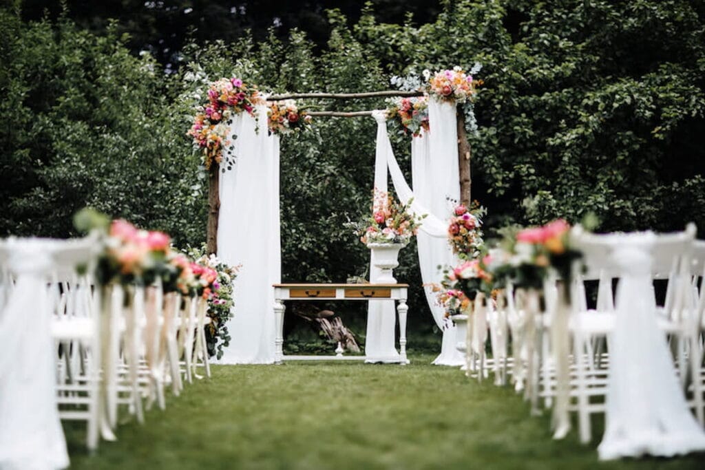 Elegant and romantic outdoor wedding ceremony with altar constructed of tree branches which are draped in white gauze and flowers