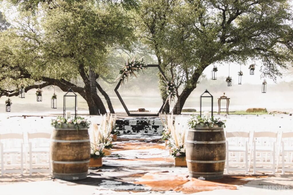 A wooden hexagon covered in flowers sits on an outdoor altar underneath trees at an outdoor wedding ceremony