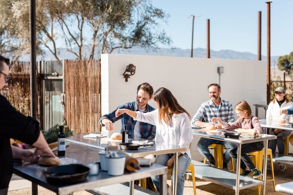 People sit at stainless steel tables at an outdoor kitchen venue taking a cooking class