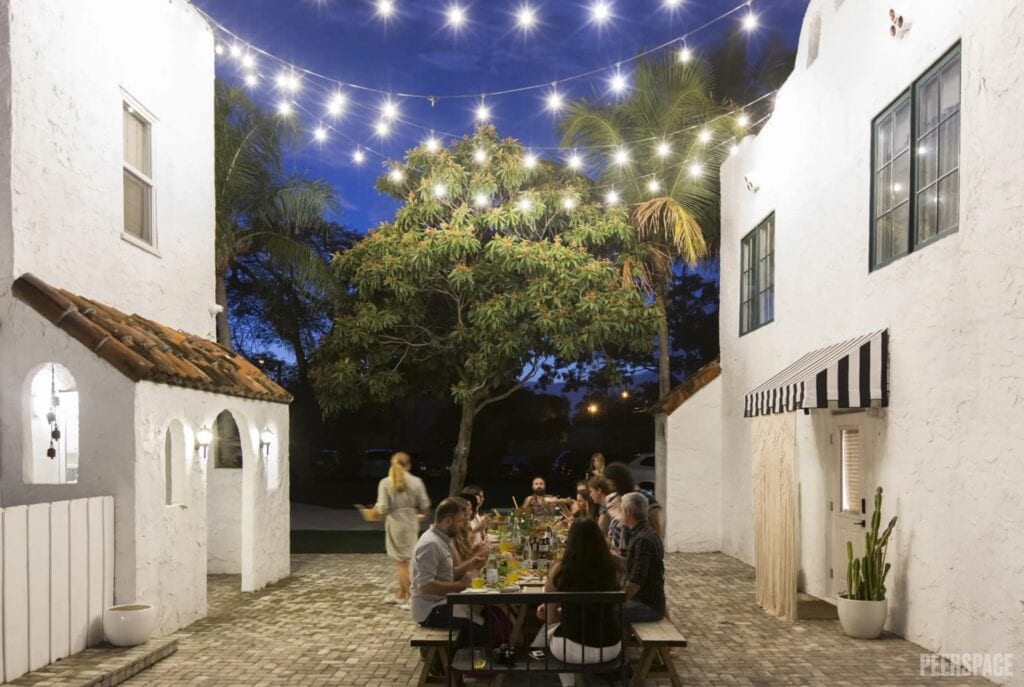 People dine under string lights in a courtyard in a tropical setting