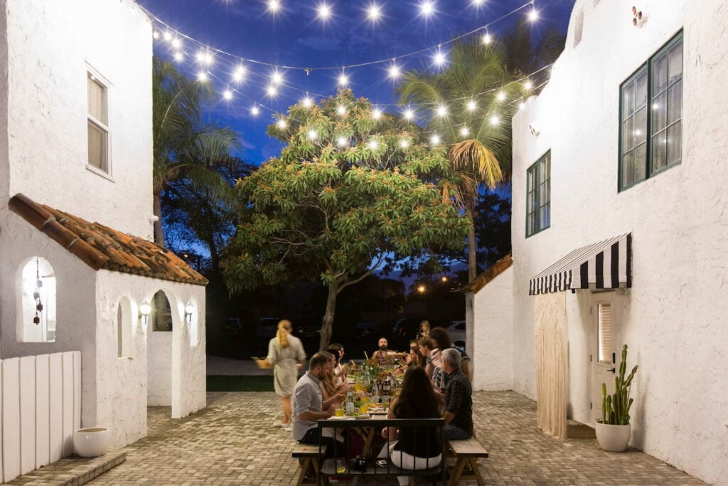 String lights illuminate a table in a courtyard where guests are having a dinner party