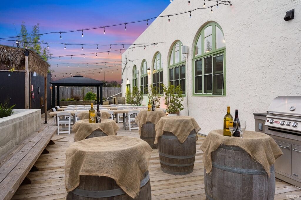 A rooftop of a converted church is set up for a party with wine barrel tables covered in burlap at dusk
