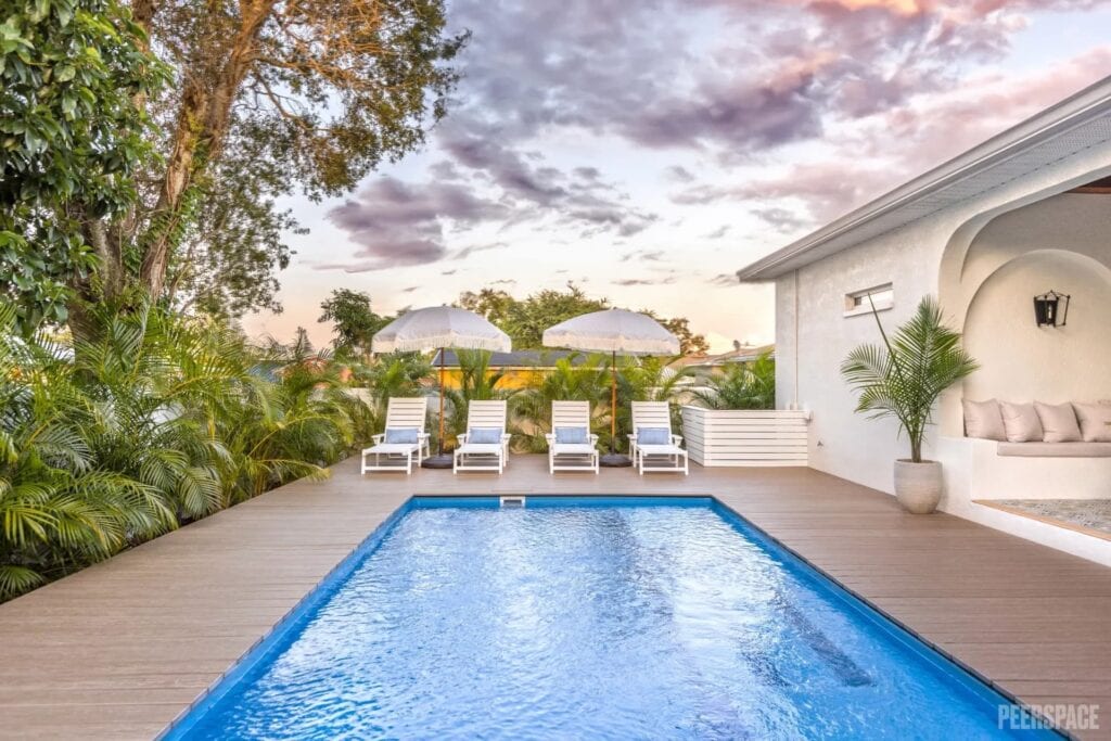 A pristine pool glistens at dusk in a private, luxe backyard surrounded by palms
