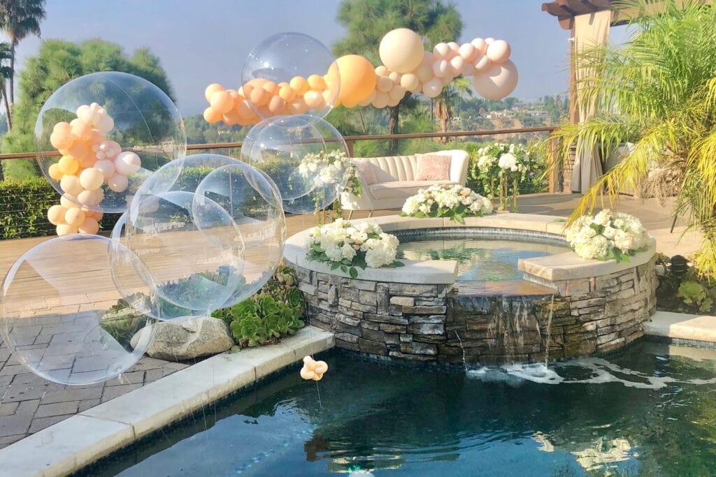 A beautiful outdoor pool area is decorated with neutral and clear balloons at a baby event