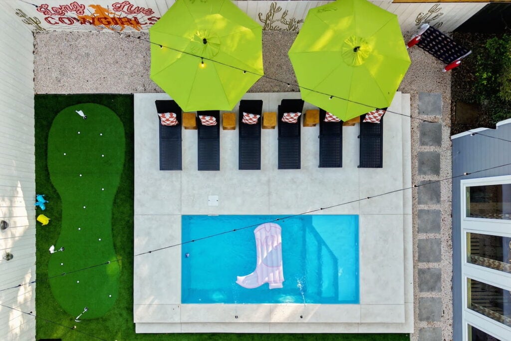 Overhead shot of a backyard pool area with a putting green, lounge chairs and a cowboy boot-shaped float