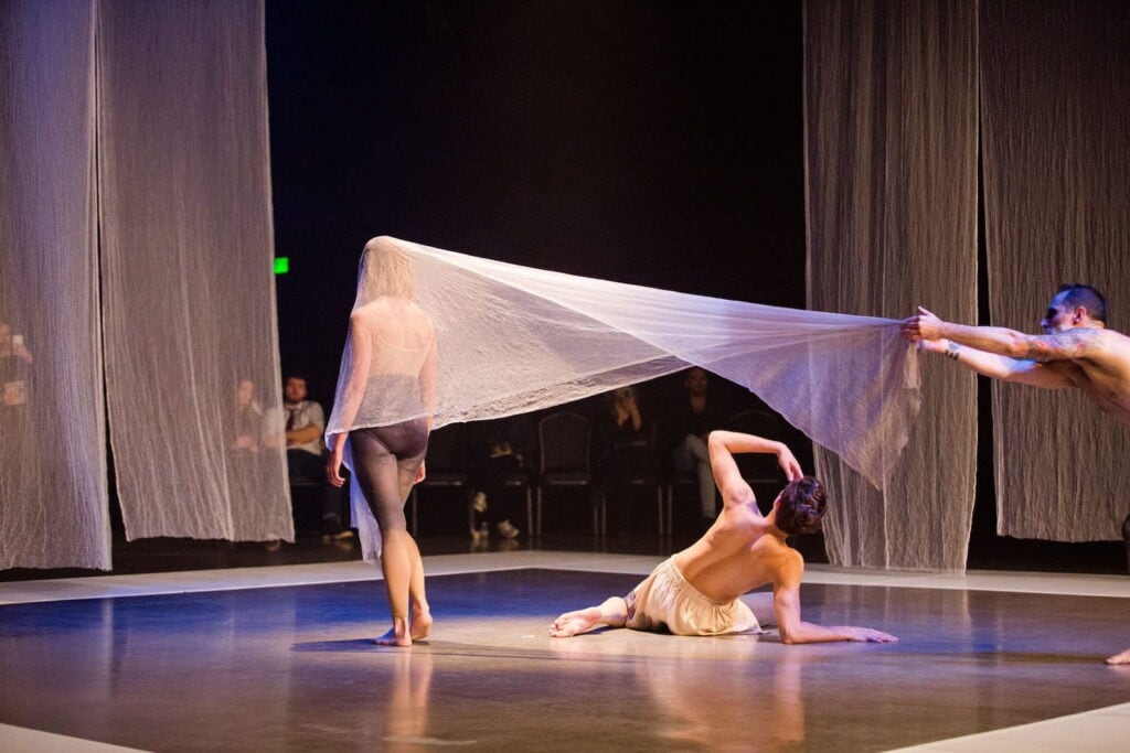 Three dancers on a stage that's surrounded by draped gauze