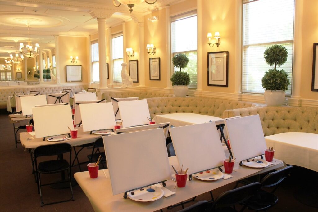 A brightly-lit, all-white restaurant space is set up with canvases for a painting party