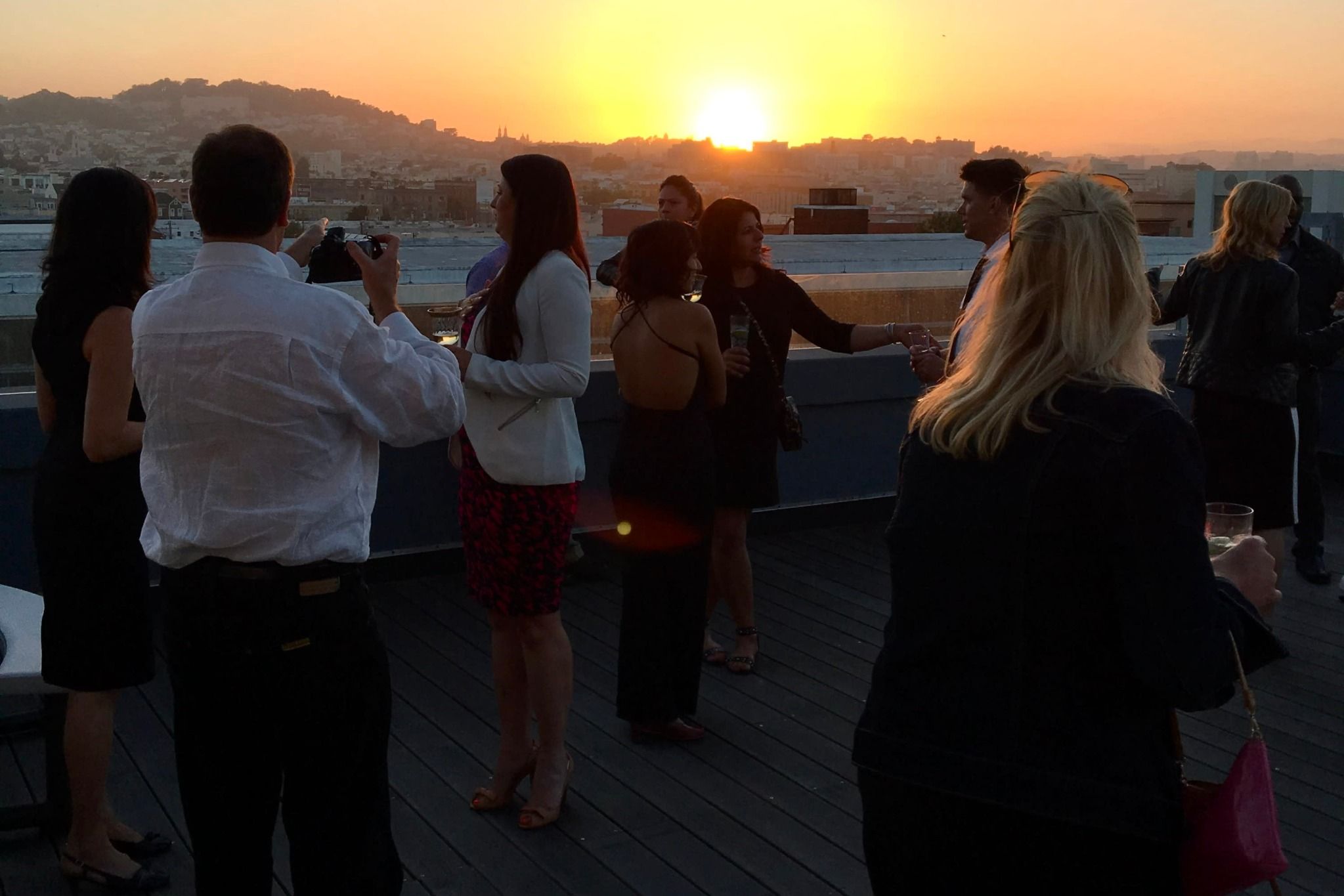 California rooftop party guests enjoying golden sunset over coastal cityscape