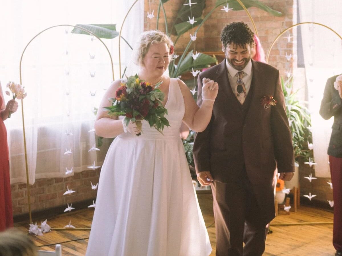Couple walking down aisle of small wedding at home with DIY backdrop