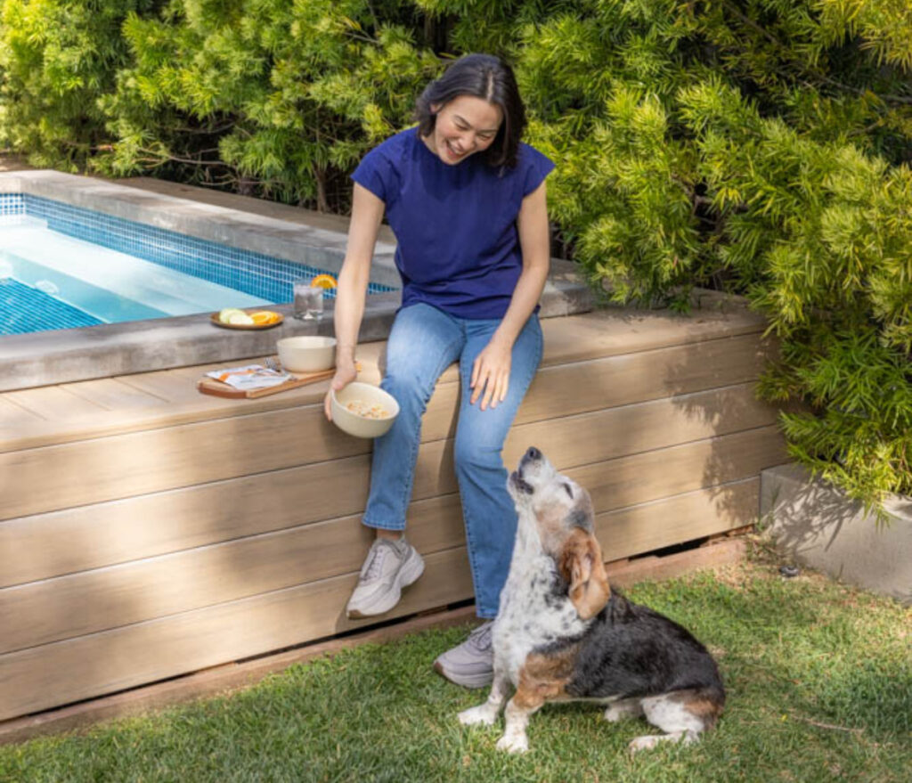 Woman sitting on edge of pool with food and small dog