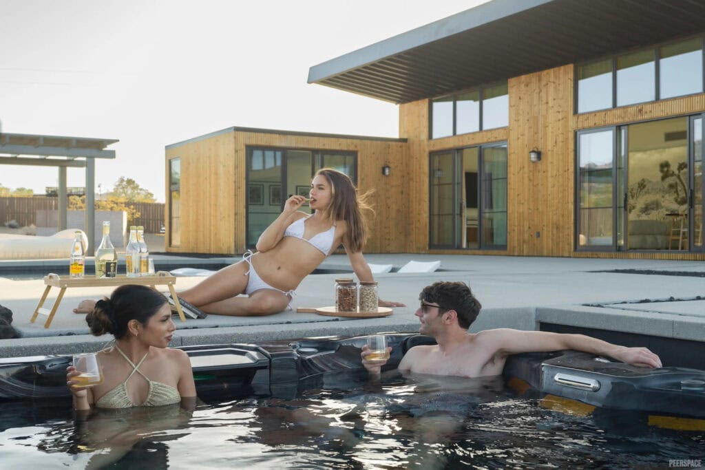 Three people sit in and around a hot tub outside a modern house