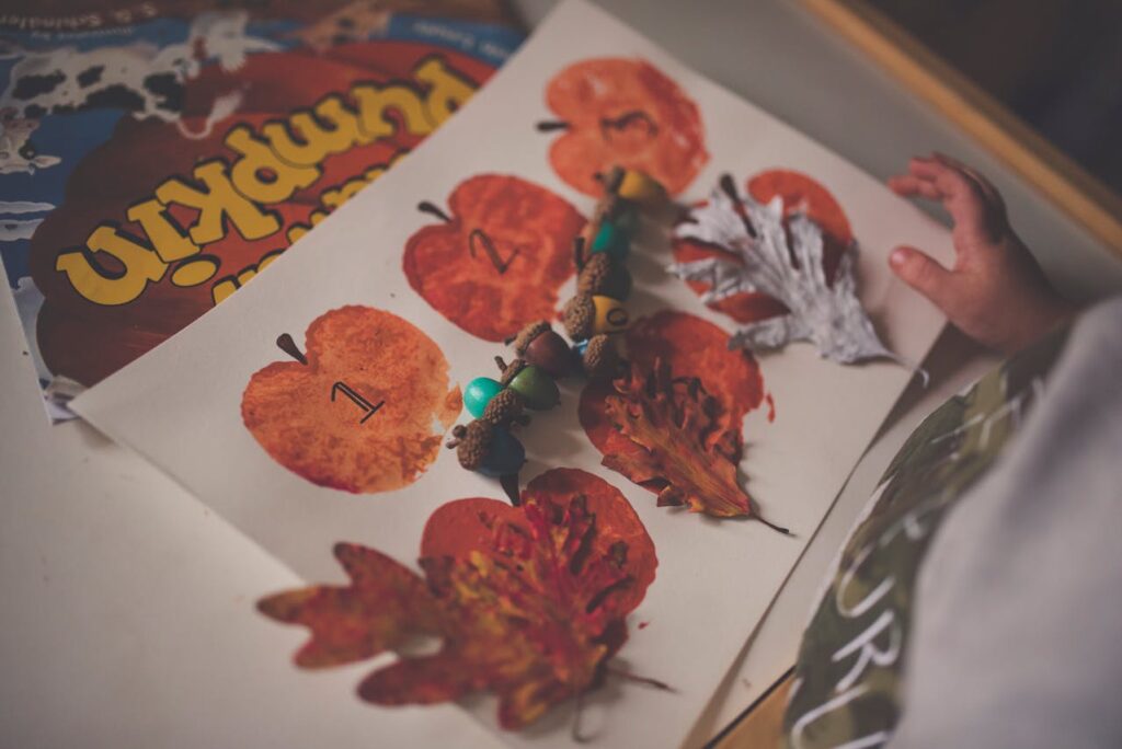 Autumn themed kids activity for Friendsgiving with dried leaves, pumpkin book, painted acorns and apples
