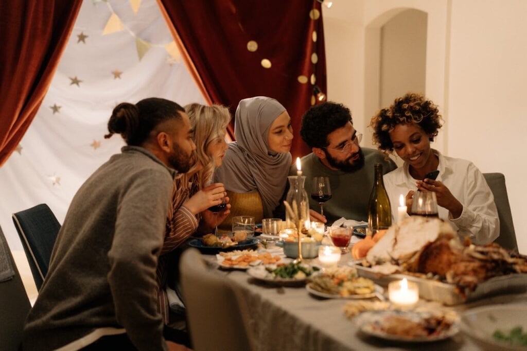 5 people sitting at a dinner table looking at one person's digital Friendsgiving gift