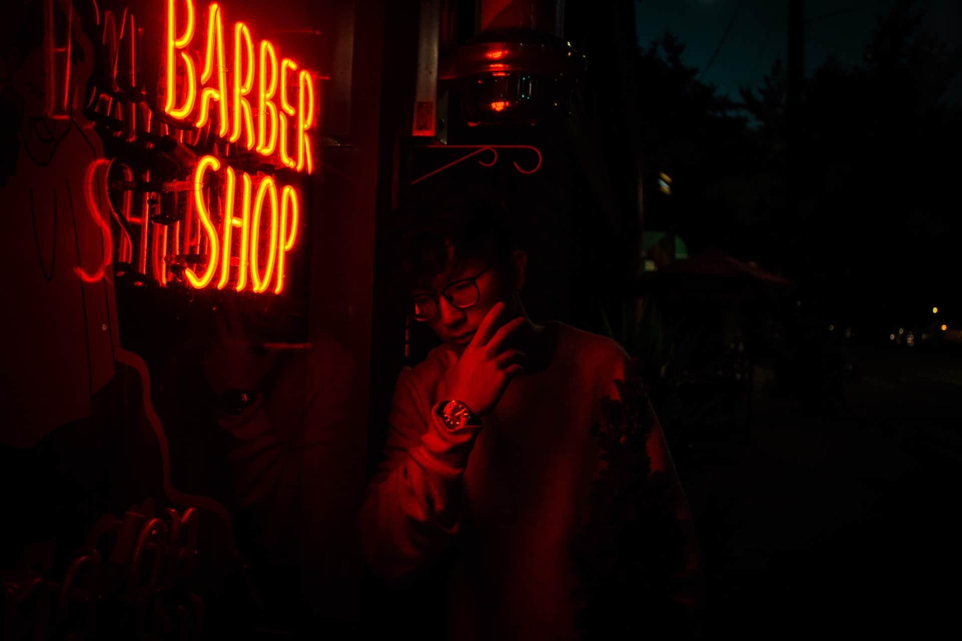 man lit by neon barber shop sign