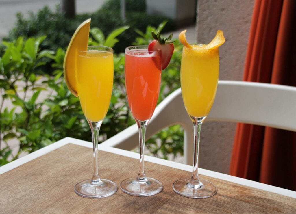 Three mimosas with juices and fruit for Galentines day ideas