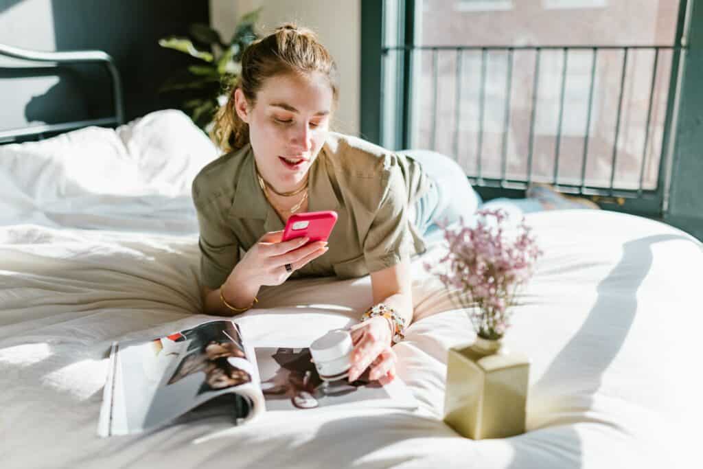 woman on bed looking at phone and magazineac