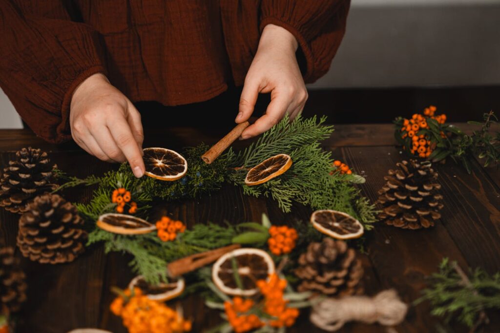 Person decorating a foraged fall decor wreath with dried oranges, cinnamon, and pinecones